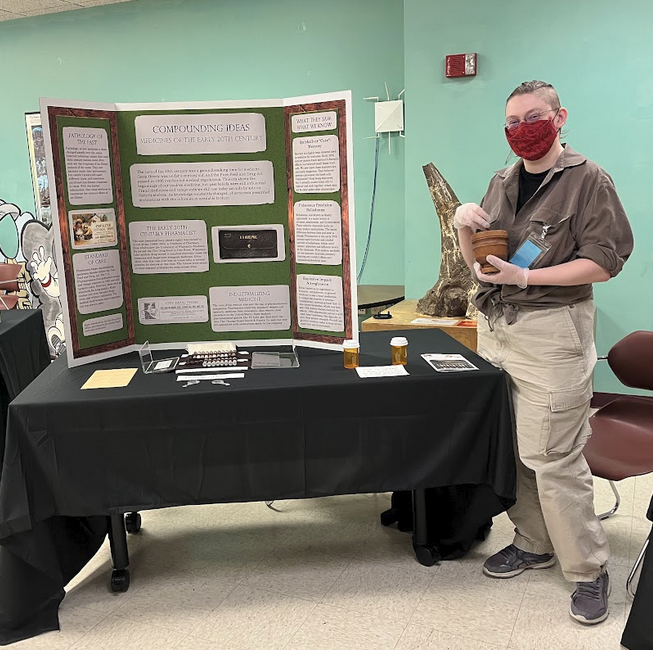A person standing in front of a trifold holding a mortar and pestle